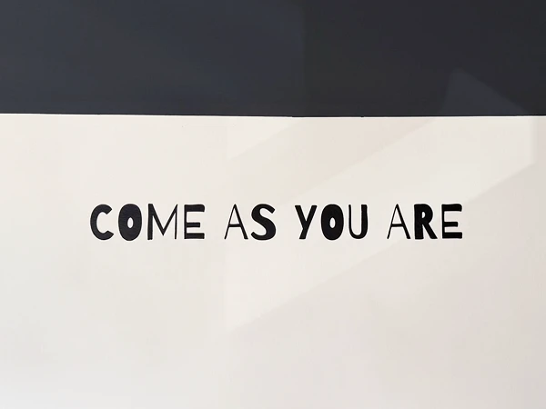 Der Schriftzug "COME AS YOU ARE" ist an einer wandfüllenden, hellen Fläche mit dunklem Hintergrund angebracht.