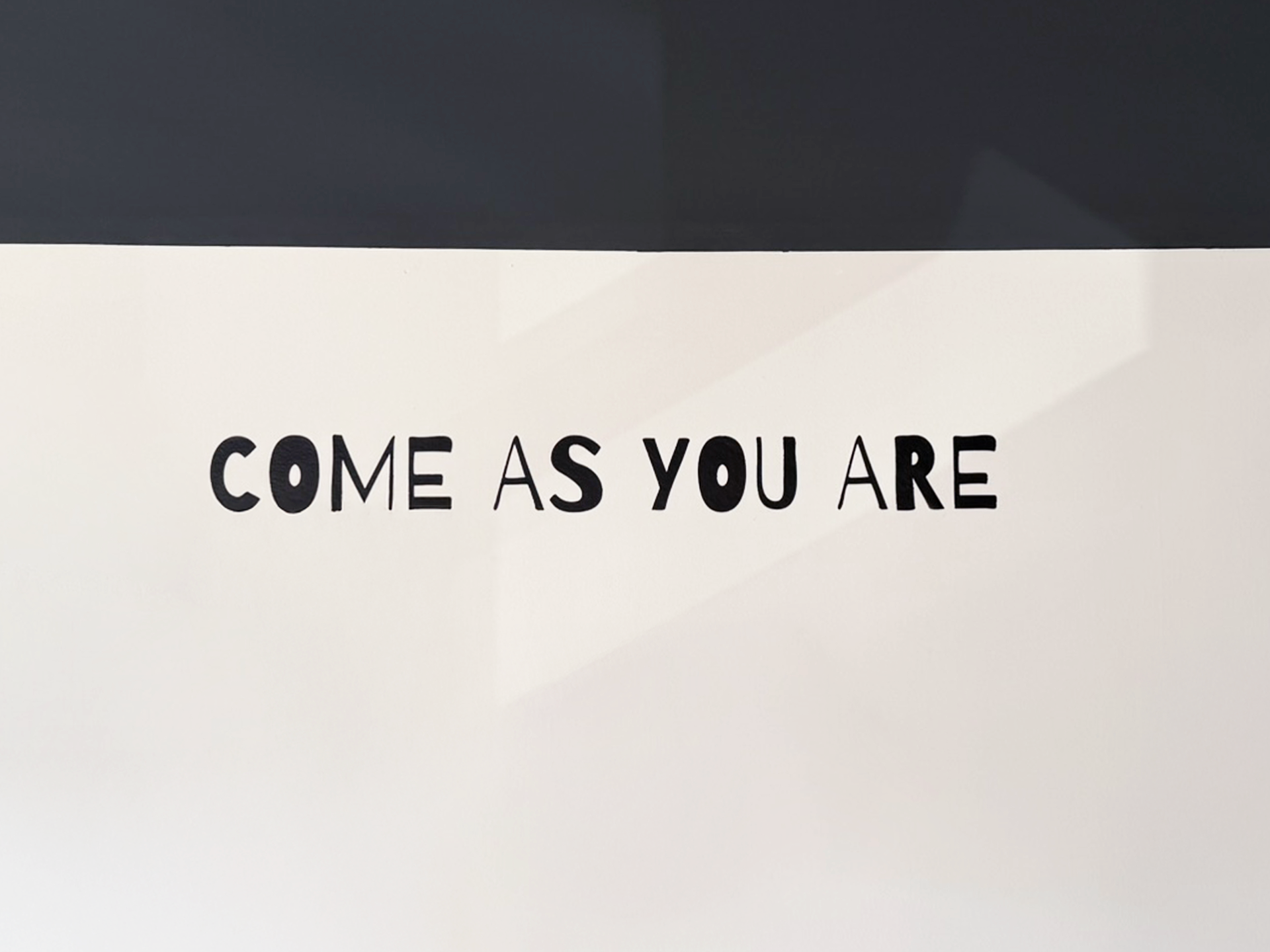 Der Schriftzug "COME AS YOU ARE" ist an einer wandfüllenden, hellen Fläche mit dunklem Hintergrund angebracht.
